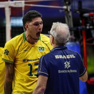 O jogador Barreto, com a camisa amarela da Seleção Brasileira, vibrando intensamente de boca aberta bem em frente ao técnico Bernardinho na beira da quadra.