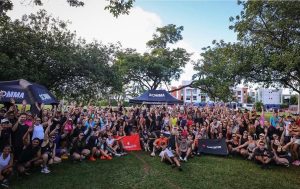 Grande grupo com dezenas de atletas de assessoria esportiva reunidos e acenando no gramado do Parque da Cidade Sarah Kubitschek em Brasília.