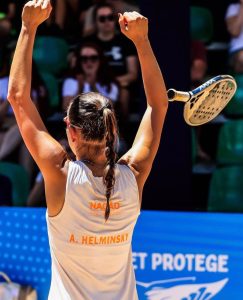 Atleta profissional Amanda Helminsky de costas, com os braços erguidos comemorando e a raquete jogada para o alto após vitória no Beach Tennis.