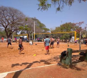 Atleras de futevôlei em quadras públicas de areia cercadas por árvores no Parque da Cidade, em Brasília, sob um céu azul.