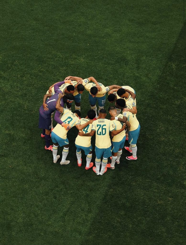 Foto aérea tirada de um ângulo zenital (totalmente de cima) mostrando onze jogadores da Seleção Brasileira de futebol masculino reunidos em um círculo perfeito (