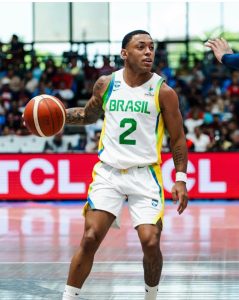 O armador Yago Mateus em quadra batendo bola com a mão direita e olhando para o ataque. Ele usa o uniforme branco da Seleção Brasileira com o número 2 em destaque.